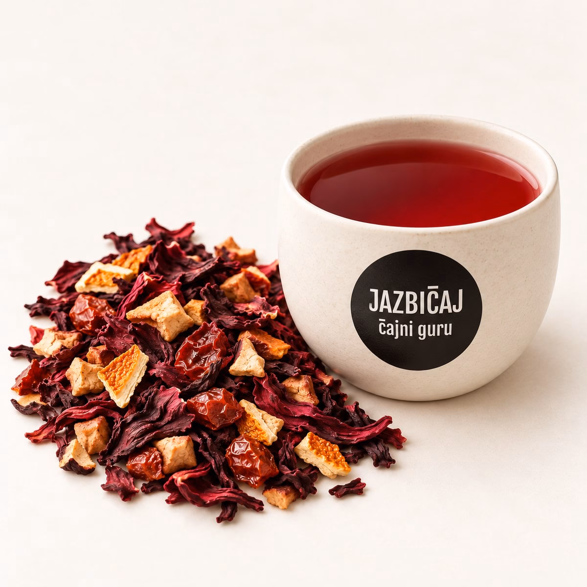Skodelica sadnega čaja z logotipom Jazbičaj ob mešanici suhega sadja in hibiskusa.